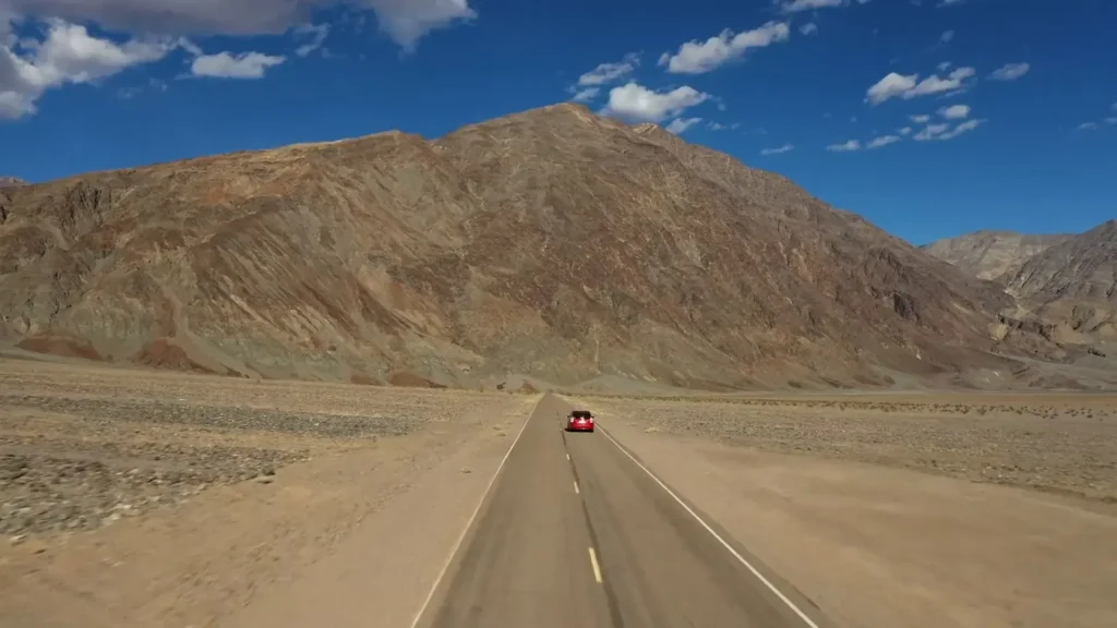 A car on a desert road below a mountain, seen from the air