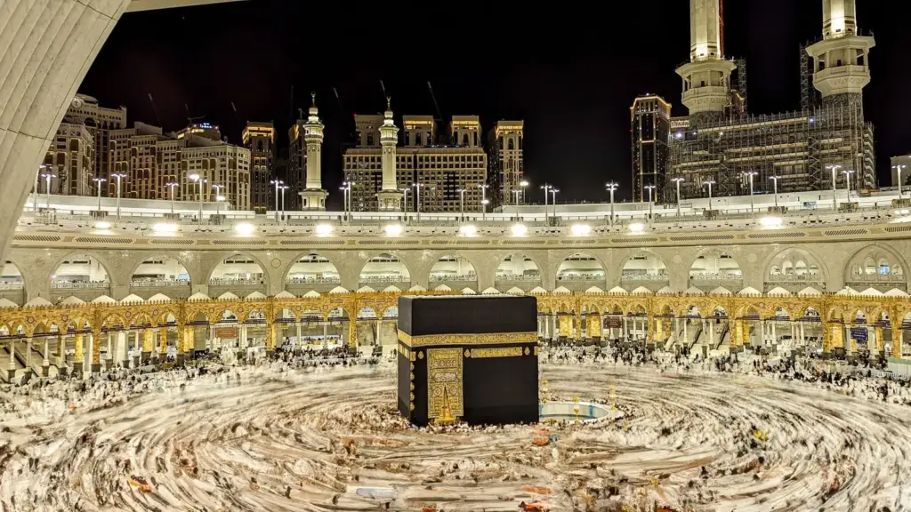 The Kaaba and the courtyard of Masjid al-Haram at night, with the clock tower behind