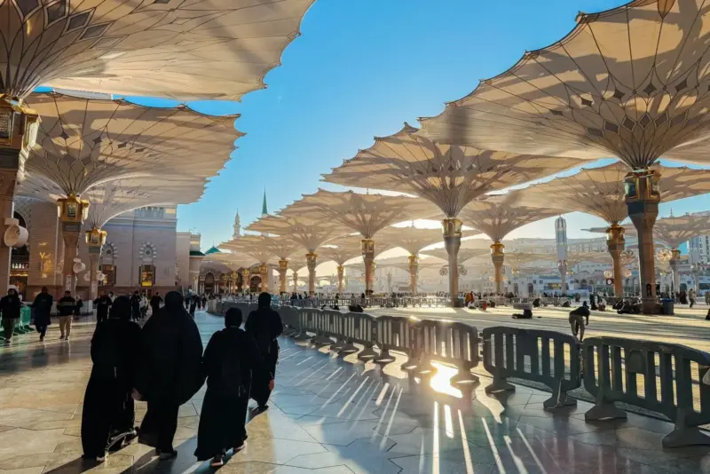 الشمس تسطع بين المظلات المفتوحة في المسجد النبوي، والزوار يمشون تحتها