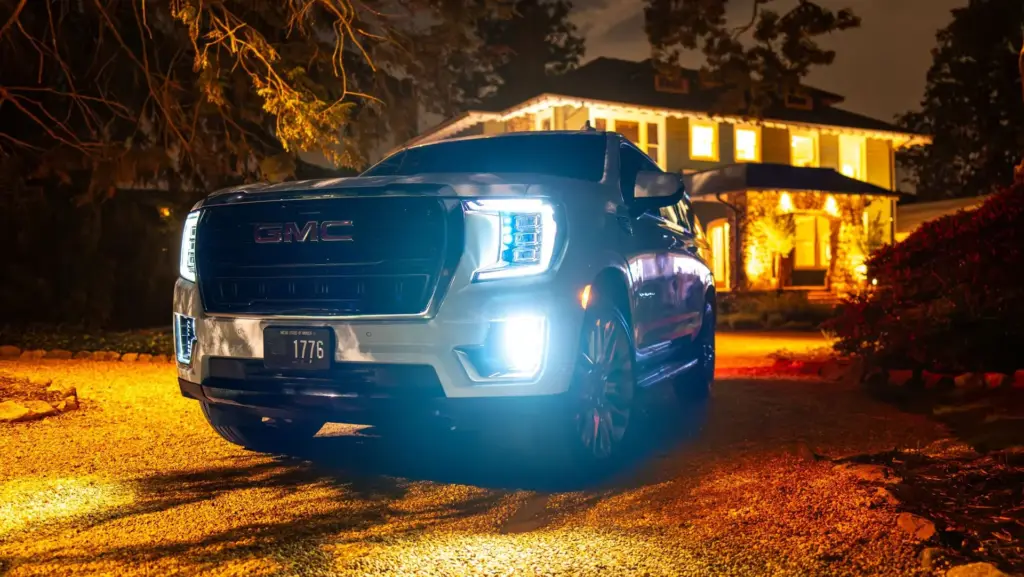 A dark GMC Yukon XL at night with its headlights on