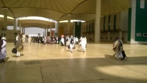 Pilgrims with bags and luggage walking under the white tent roof of the Hajj Terminal, King Abdulaziz International Airport, Jeddah