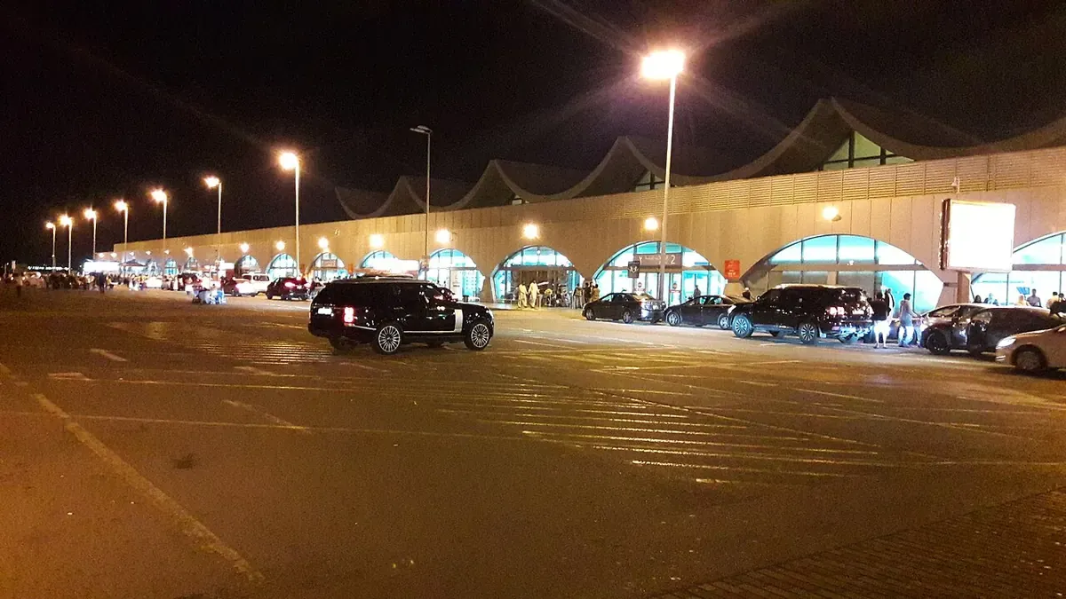North Terminal of King Abdulaziz International Airport, Jeddah, at night, with its wave shaped roof and cars at the kerb
