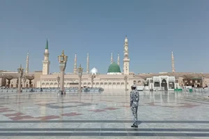 Courtyard of Masjid an-Nabawi, Madinah, with the Green Dome and minarets and a guard standing on the marble