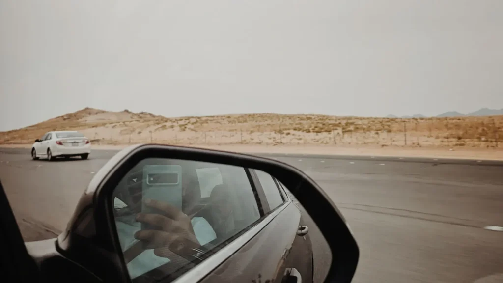 Desert highway and sand dunes seen in a car side mirror in Saudi Arabia; the exact road is not stated