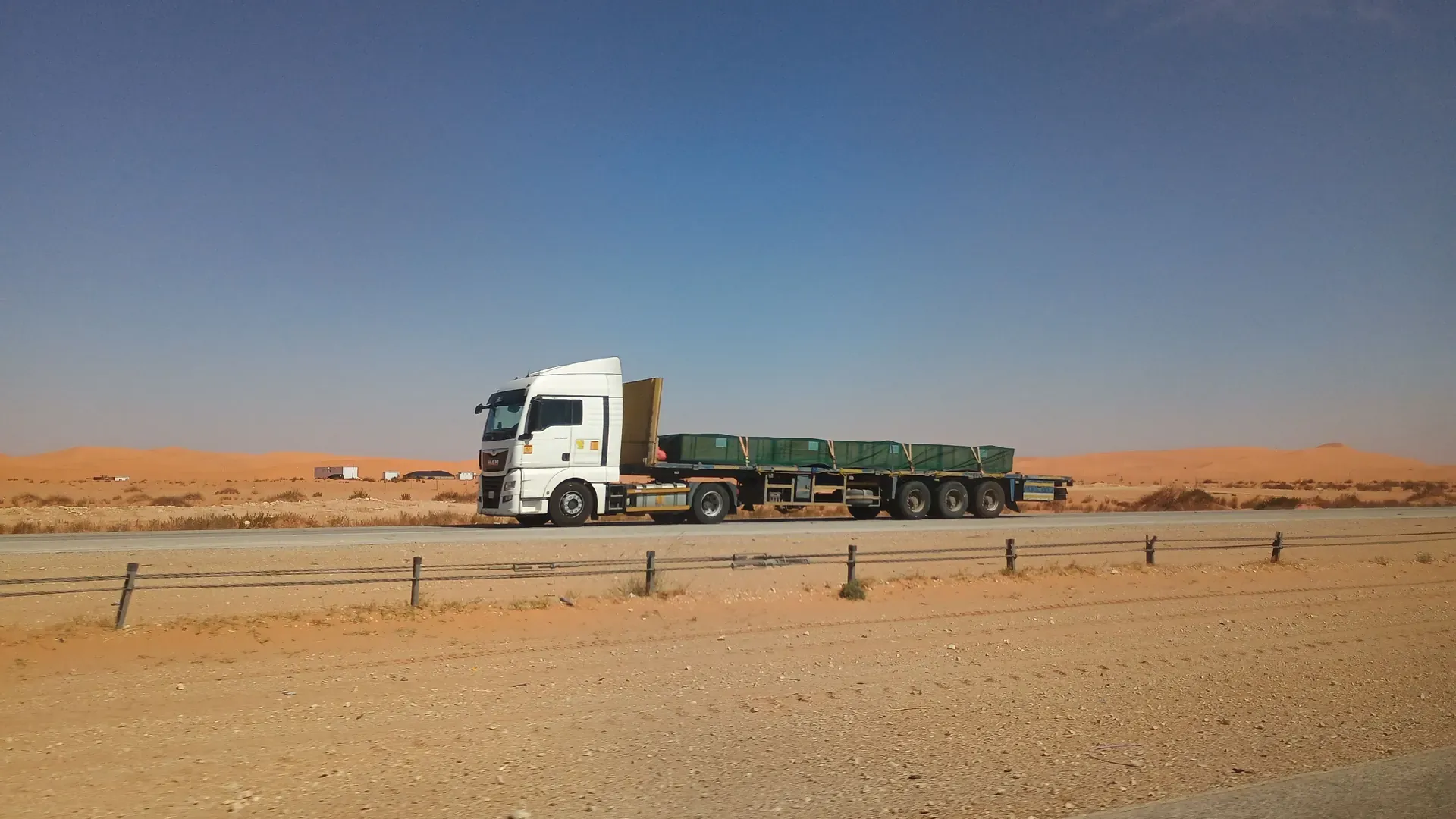 Flatbed truck on an empty desert highway in Saudi Arabia under a clear sky; Eastern Province, not on a Makkah or Madinah route