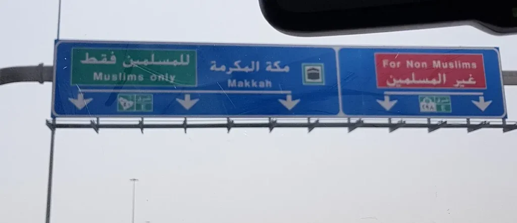 Blue overhead sign on the Jeddah to Makkah highway: Muslims only lanes to Makkah and the exit for non Muslims, in Arabic and English