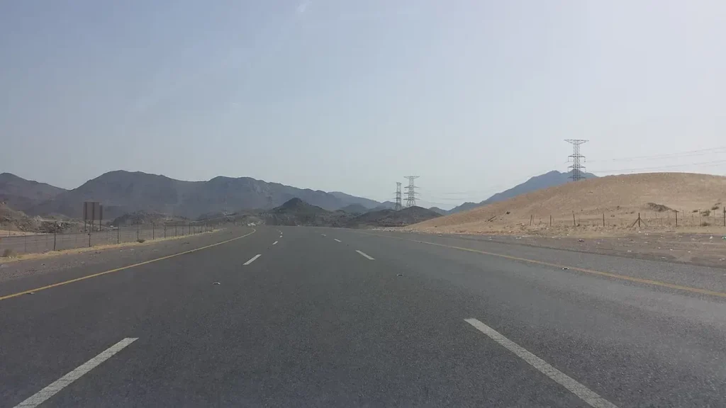 Empty divided highway toward Madinah through desert hills with power pylons