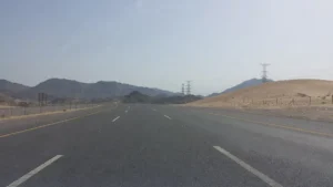 Empty divided highway toward Madinah through desert hills with power pylons