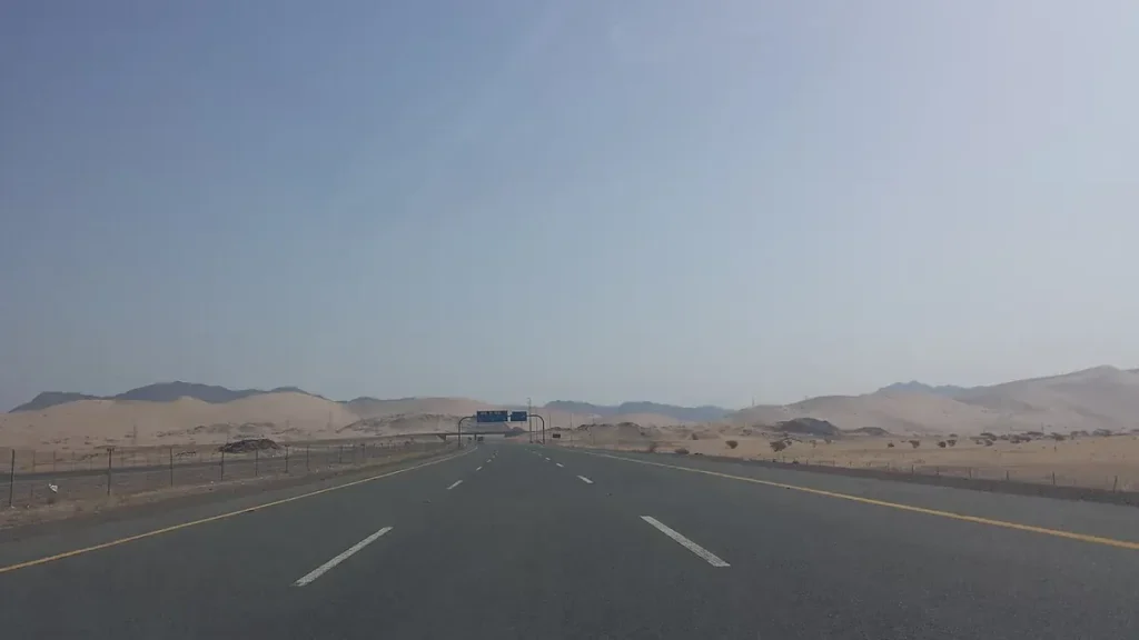 Wide highway through sand and hills in Al Madinah Province, with an overhead sign gantry ahead