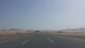 Wide highway through sand and hills in Al Madinah Province, with an overhead sign gantry ahead
