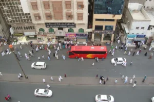 Ibrahim Al Khalil Road, Makkah, from above: pilgrims crossing, a red bus and cars in front of hotels including Al Reyadah Grand Hotel