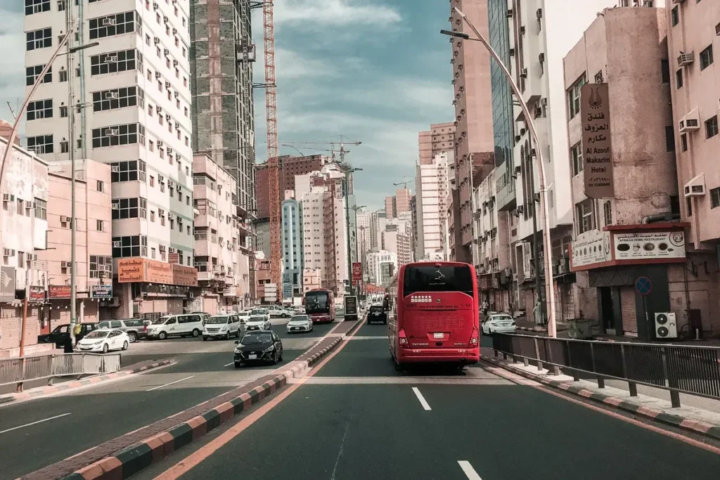 Busy Makkah street with hotels, cars and a red bus, seen from inside a car