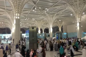 Crowd of pilgrims with trolleys inside the terminal of Prince Mohammad bin Abdulaziz Airport, Madinah, under its white tree shaped columns
