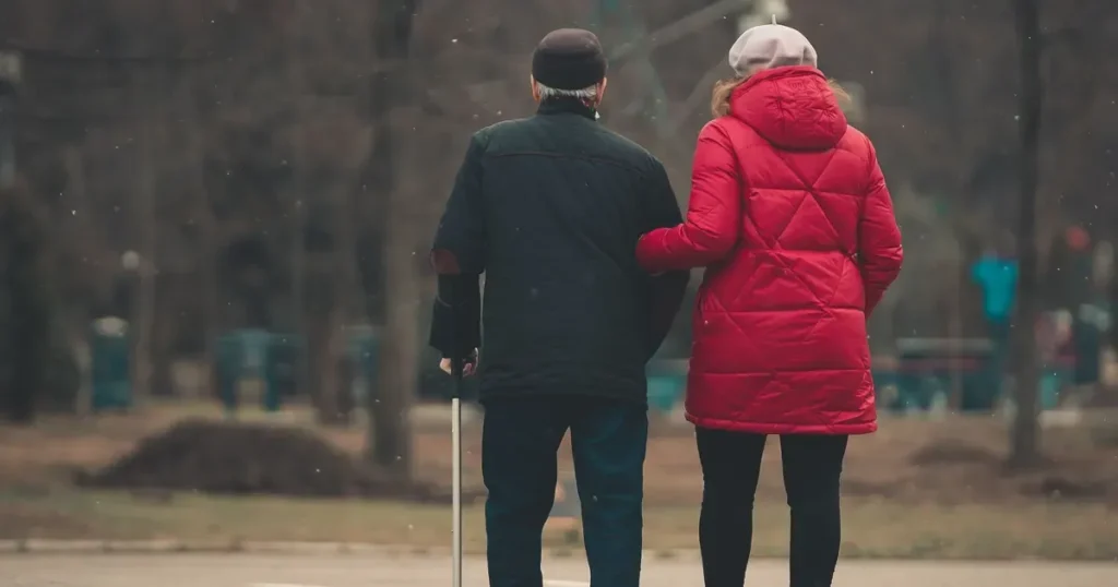 Elderly couple walking arm in arm with a cane, seen from behind; generic, not a Saudi location