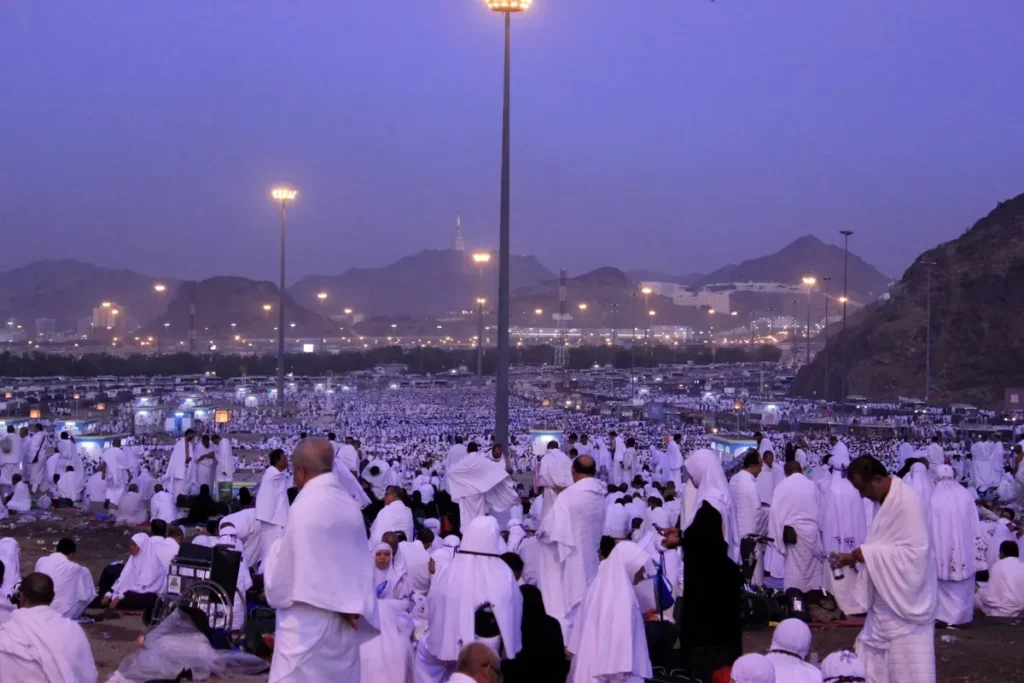 Pilgrims at Muzdalifah at dawn with lights and mountains