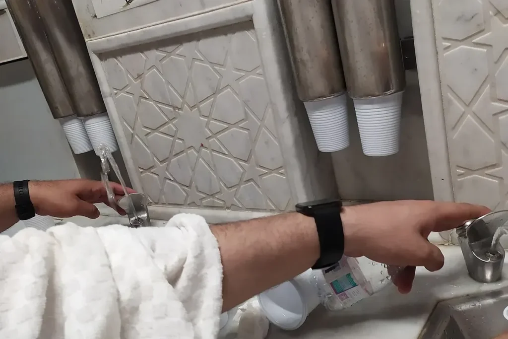 Zamzam water taps with cups at a Zamzam drinking point in Masjid al-Haram, Makkah, hands only