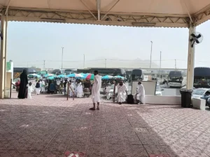 The shaded forecourt of Masjid al-Jiranah with pilgrims in ihram and coaches beyond