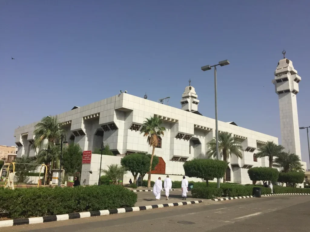 The long white front of Masjid Aisha at Taneem with visitors in ihram walking in