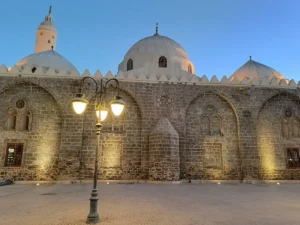 The domes and stone front of Masjid al-Ghamama lit in the evening