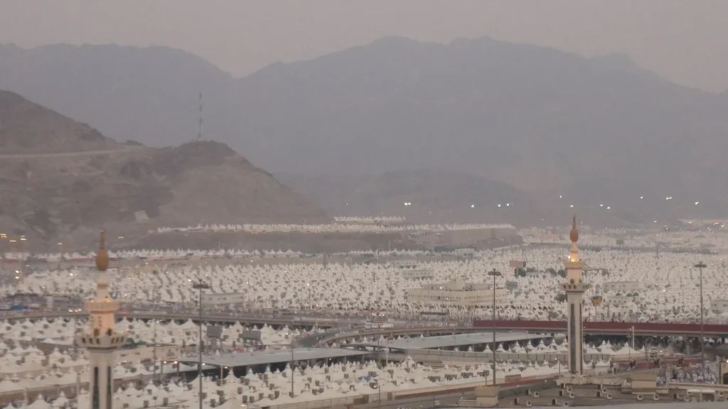 The white tent city of Mina filling the valley below the mountains, with mosque minarets among the tents