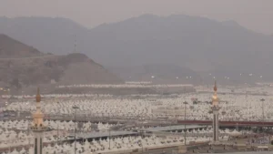 The white tent city of Mina filling the valley below the mountains, with mosque minarets among the tents