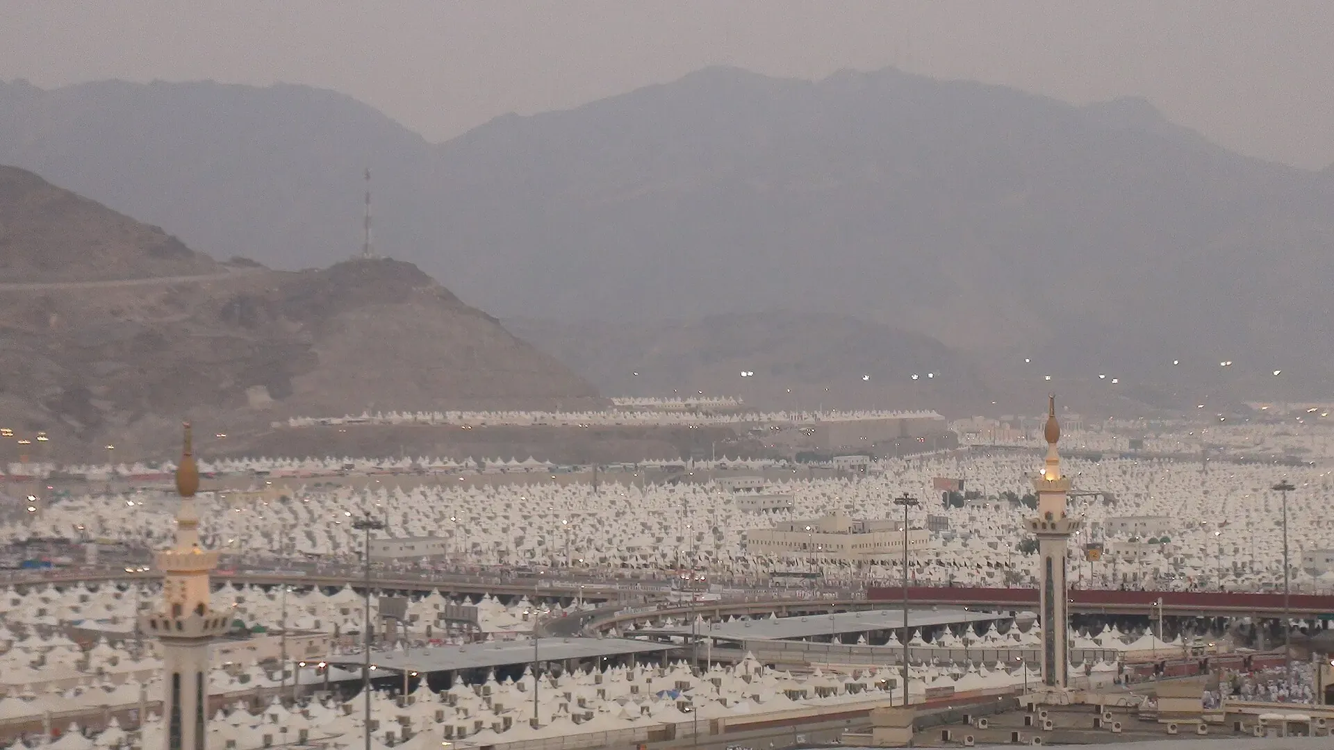 The white tent city of Mina filling the valley below the mountains, with mosque minarets among the tents