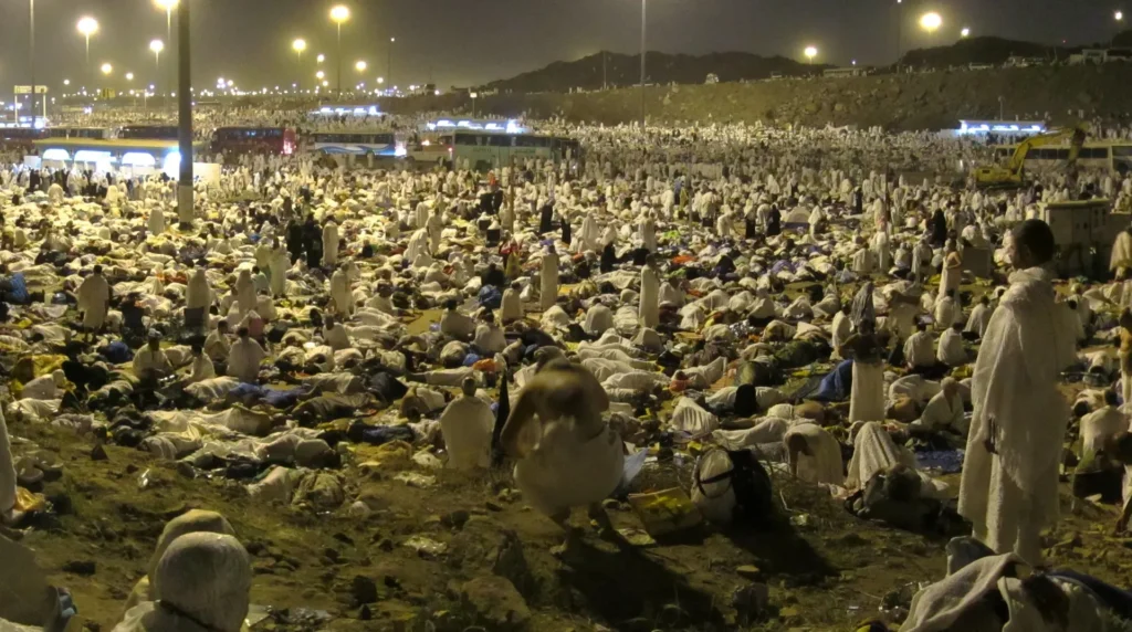 Pilgrims resting on the open ground of Muzdalifah at night under floodlights
