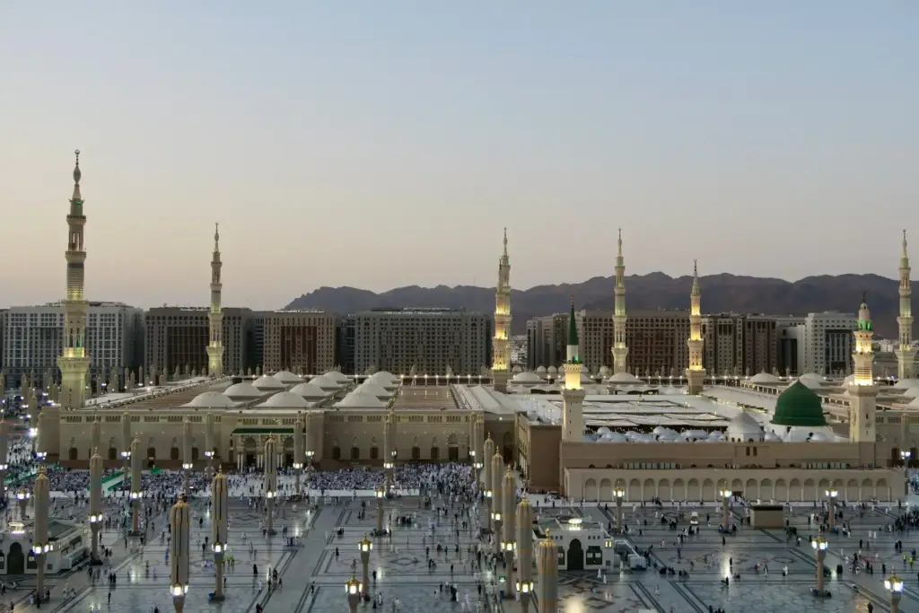 Masjid an-Nabawi and its courtyard at dusk with the mountains of Madinah behind