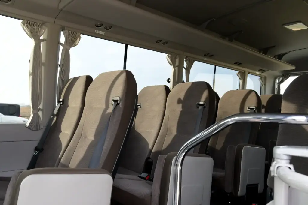 Rows of empty grey passenger seats with seat belts inside a Toyota Coaster minibus